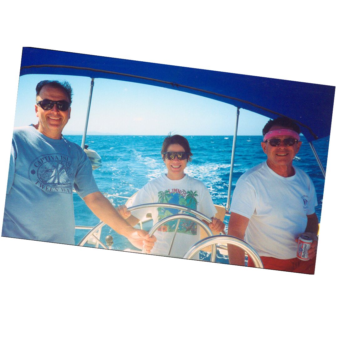 David and Jan Irons, along with Dave Shearlock, around the wheel of a sailboat, grinning with the joy of sailing