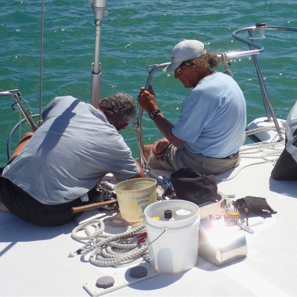 Two men doing maintenance on bow of sailboat