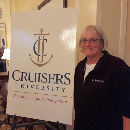 Carolyn Shearlock standing next to a Cruisers University sign, representing the launch of The Boat Galley's online courses on the timeline.