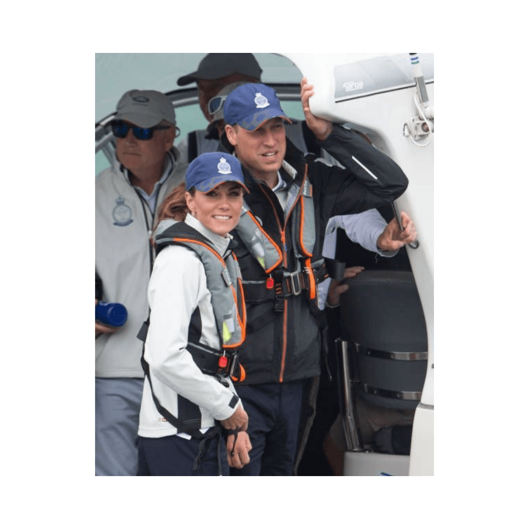 Two people in blue caps and sailing gear stand by a boat’s entrance, both wearing Cruising Solutions' TeamO PFD with BackTow™ – Offshore Black Hammar. Others in similar PFDs are seen nearby, getting ready for a boating activity.
